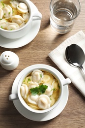 Photo of Tasty dumplings in broth served on wooden table, top view