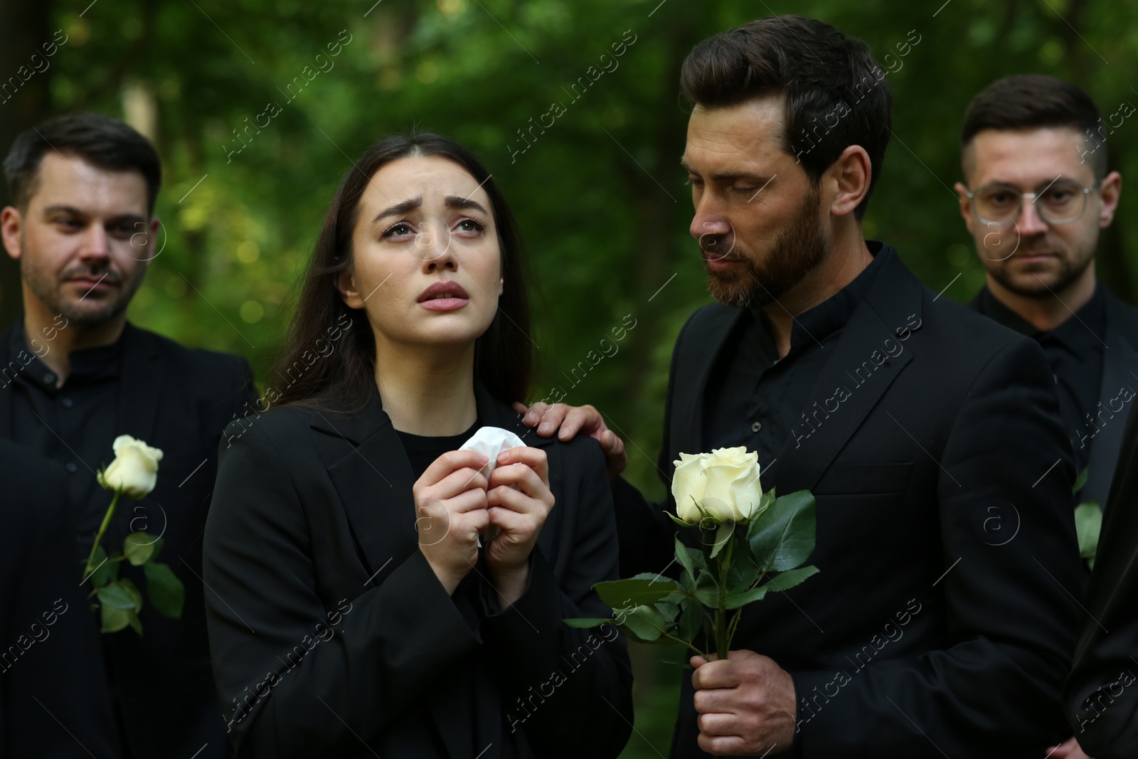 Photo of Funeral ceremony. Sad people with white rose flowers mourning outdoors