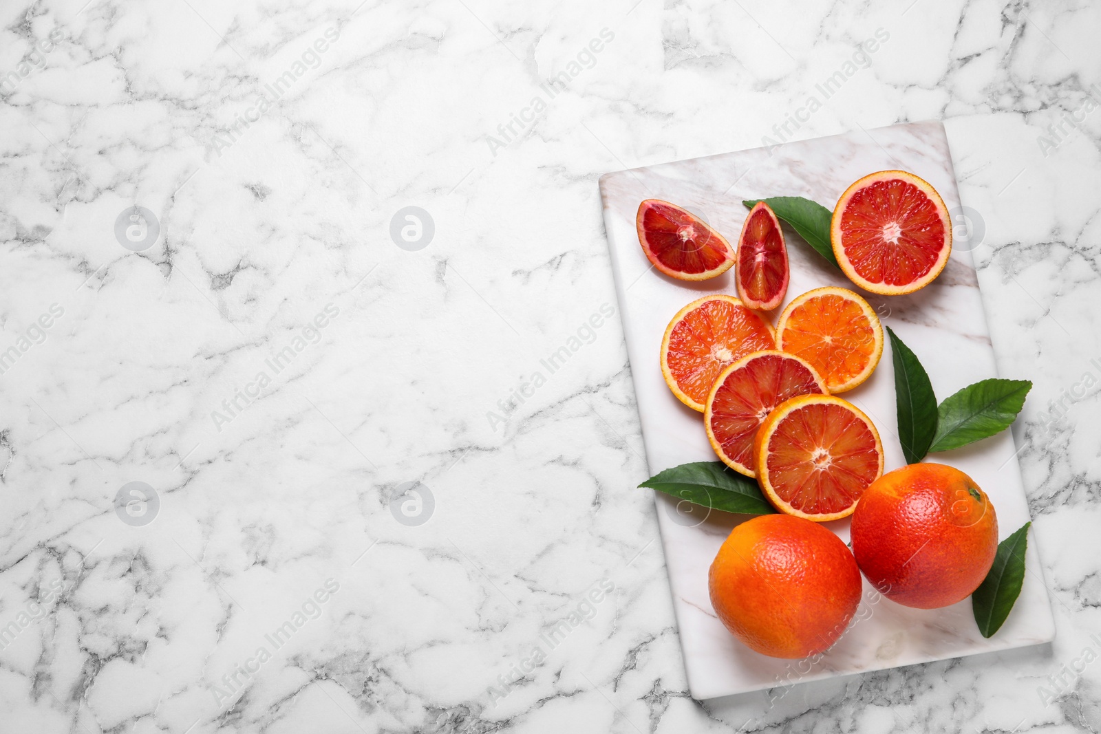 Photo of Whole and cut red oranges on white marble table, top view. Space for text