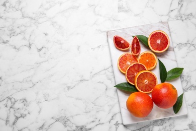 Whole and cut red oranges on white marble table, top view. Space for text