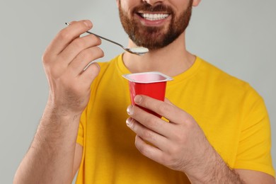 Man with delicious yogurt on light grey background, closeup