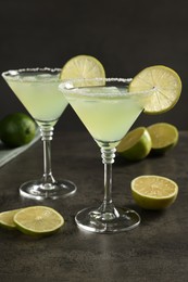 Delicious Margarita cocktail with ice cubes in glasses and limes on grey table