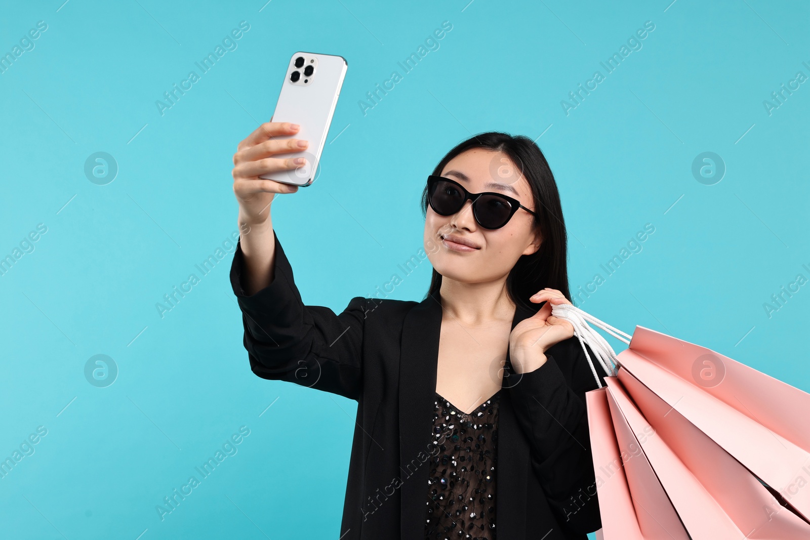 Photo of Beautiful woman with shopping bags taking selfie on light blue background. Space for text