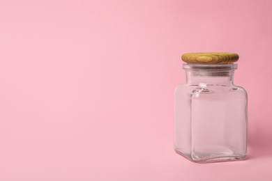 Closed empty glass jar on pink background, space for text