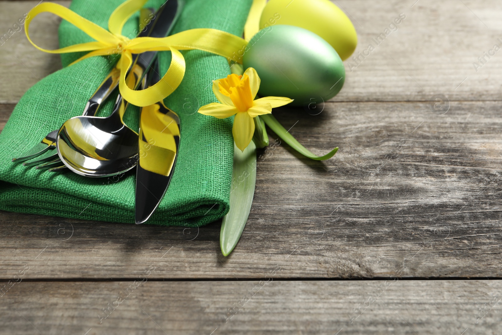 Photo of Cutlery set, painted eggs and beautiful flower on wooden table, closeup with space for text. Easter celebration