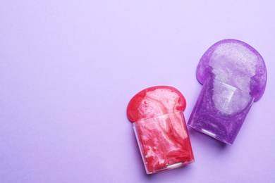 Overturned plastic containers with bright slimes on violet background, top view. Space for text