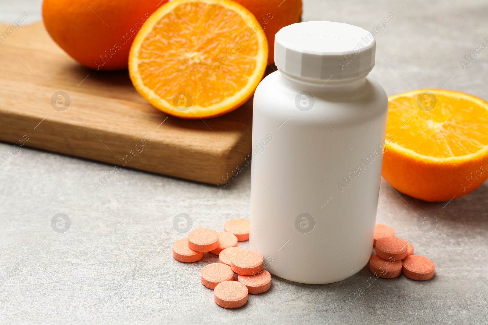 Photo of Dietary supplements. Plastic bottle, pills and oranges on grey table