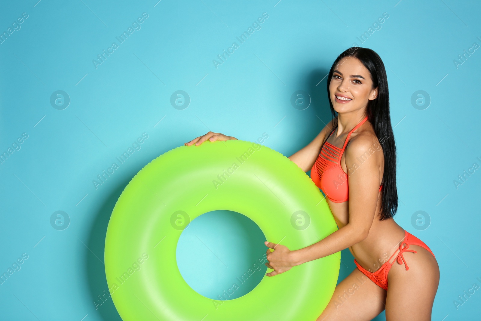 Photo of Beautiful young woman in stylish bikini with green inflatable ring on light blue background