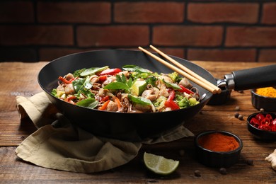 Photo of Stir-fry. Tasty noodles with meat in wok, chopsticks and ingredients on wooden table