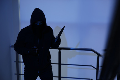 Photo of Man in mask with knife on stairs indoors, space for text. Dangerous criminal