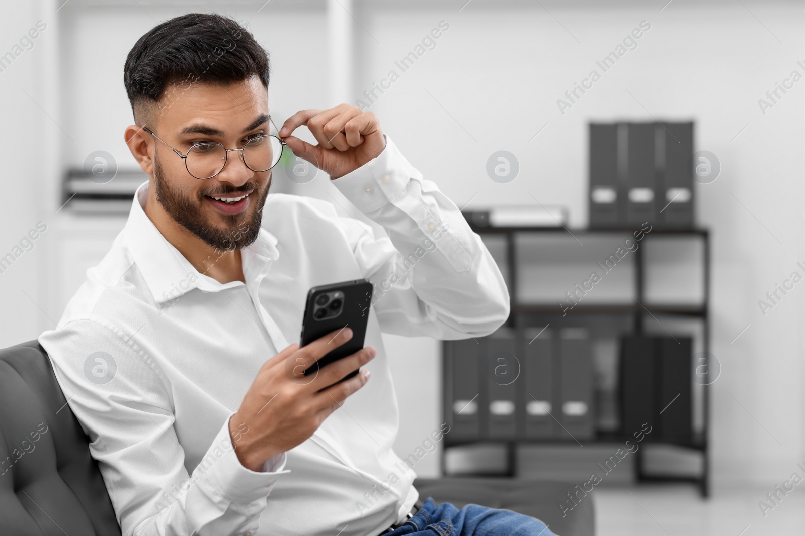 Photo of Happy young man using smartphone in office, space for text