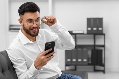 Photo of Happy young man using smartphone in office, space for text