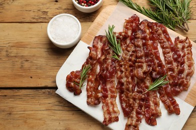 Photo of Slices of tasty fried bacon, rosemary and salt on wooden table, top view