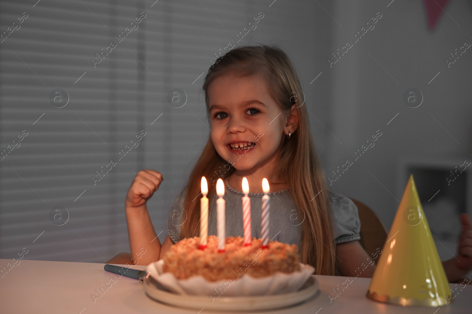 Photo of Cute girl with birthday cake at table indoors