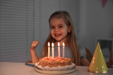 Photo of Cute girl with birthday cake at table indoors