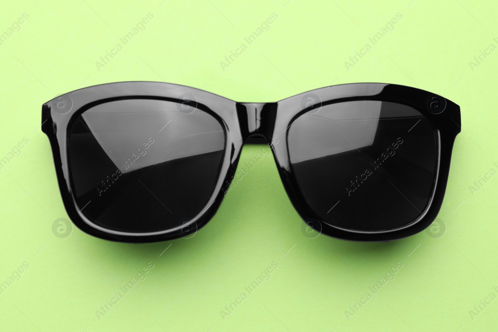 Photo of Stylish sunglasses on pale green background, top view