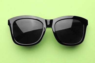 Photo of Stylish sunglasses on pale green background, top view