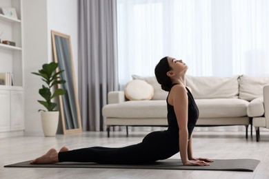 Photo of Girl practicing cobra asana on yoga mat at home. Bhujangasana pose