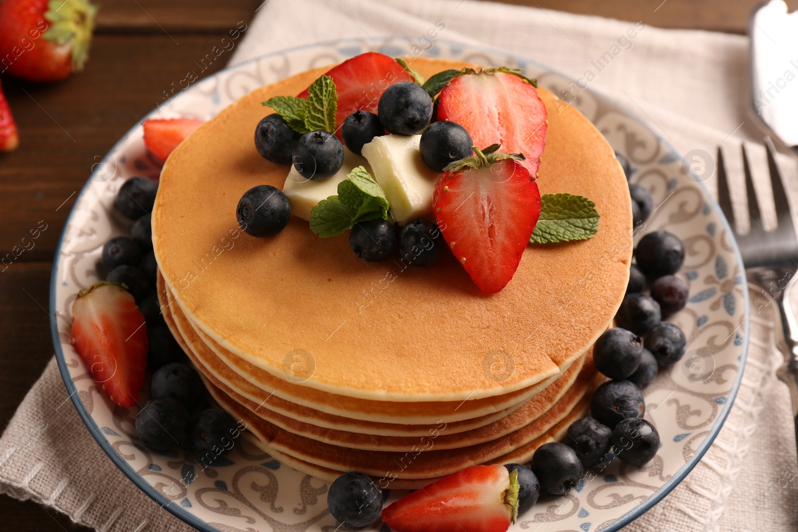 Photo of Delicious pancakes with fresh berries and butter served on wooden table, closeup