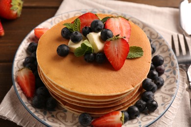 Photo of Delicious pancakes with fresh berries and butter served on wooden table, closeup