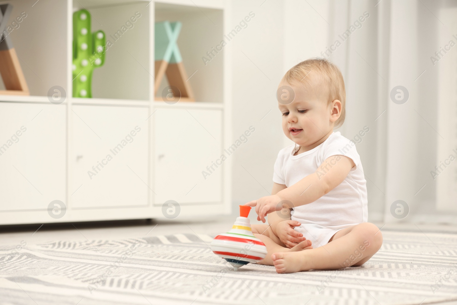 Photo of Children toys. Cute little boy playing with spinning top on rug at home, space for text