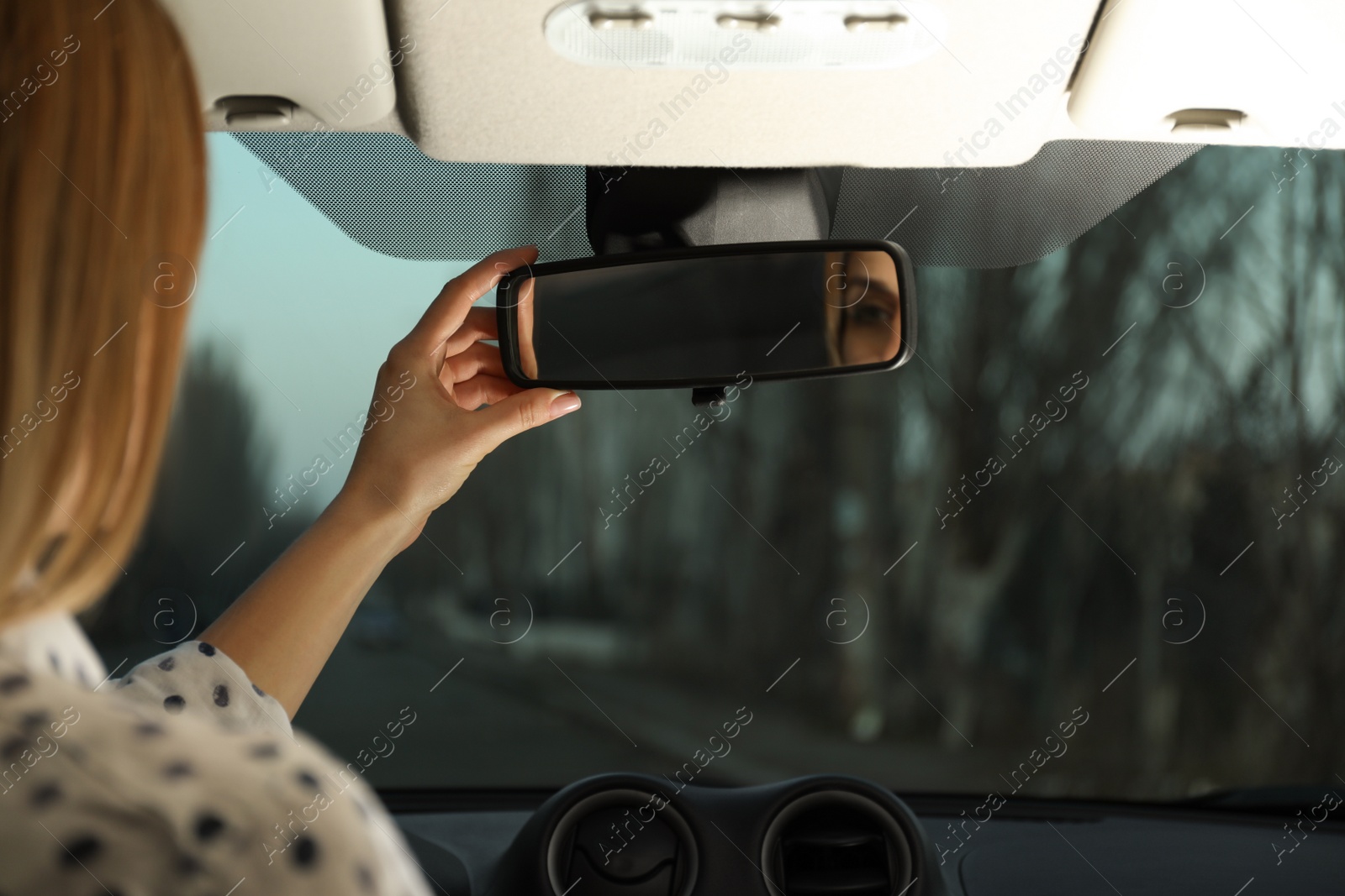 Photo of Young woman adjusting rear view mirror in car, closeup