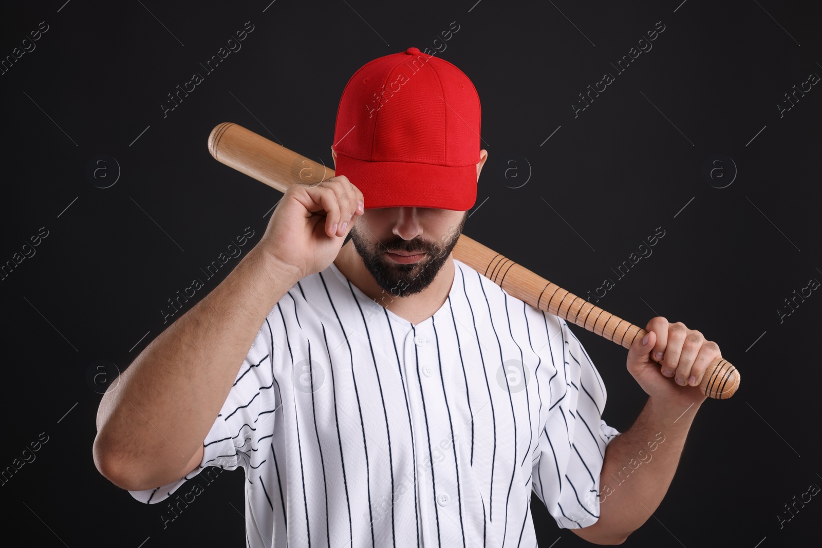 Photo of Man in stylish red baseball cap holding bat on black background