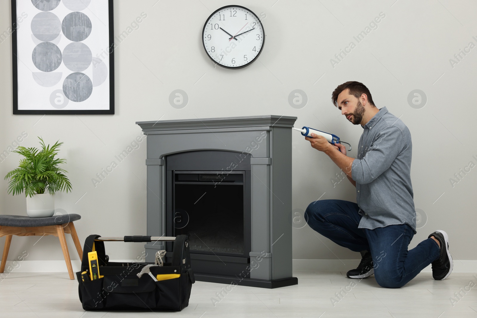 Photo of Man sealing electric fireplace with caulk near wall in room