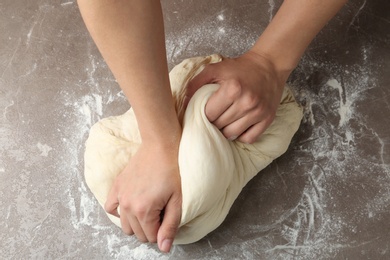 Photo of Female baker preparing bread dough at grey table, top view