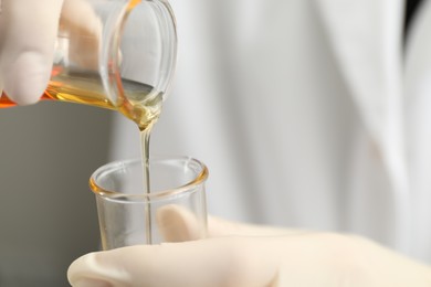 Laboratory worker pouring orange crude oil into flask, closeup