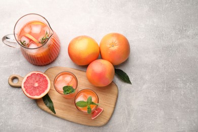 Photo of Tasty freshly made grapefruit juice, fruits and mint on light grey table, flat lay. Space for text