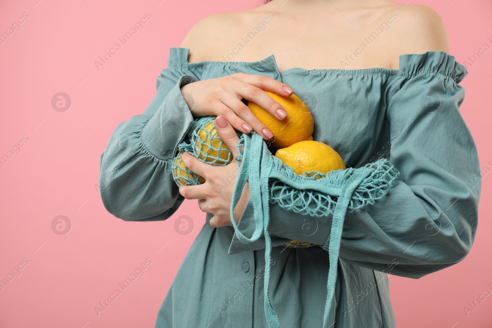 Photo of Woman with string bag of fresh lemons on pink background, closeup