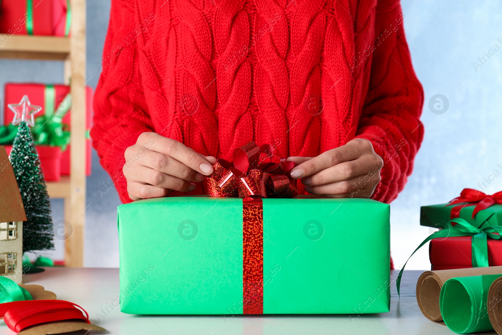 Photo of Woman wrapping Christmas gift at white wooden table indoors, closeup