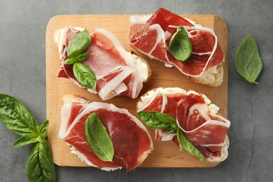 Tasty sandwiches with cured ham and basil on grey table, flat lay