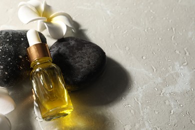 Photo of Bottle of face serum, spa stones and flower on wet grey table, space for text
