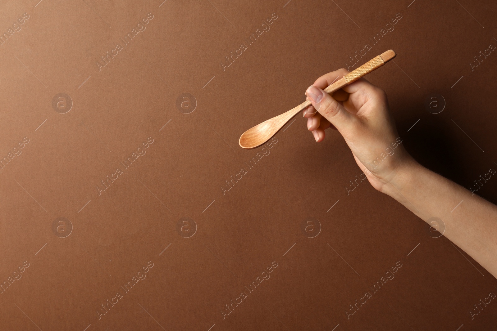 Photo of Woman holding empty wooden spoon on color background, closeup. Space for text