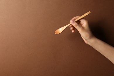 Woman holding empty wooden spoon on color background, closeup. Space for text