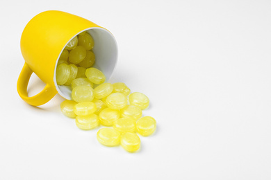 Delicious lemon drops and cup on white background