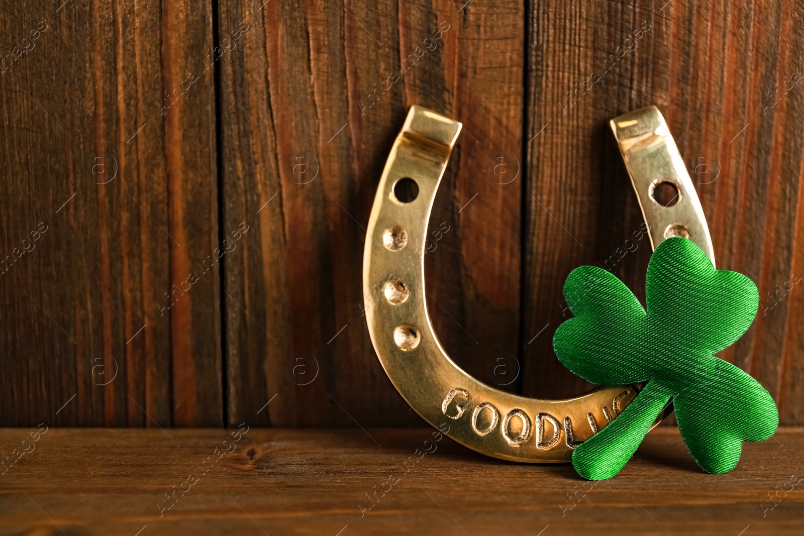 Photo of Golden horseshoe and decorative clover leaf on wooden background, space for text. Saint Patrick's Day celebration