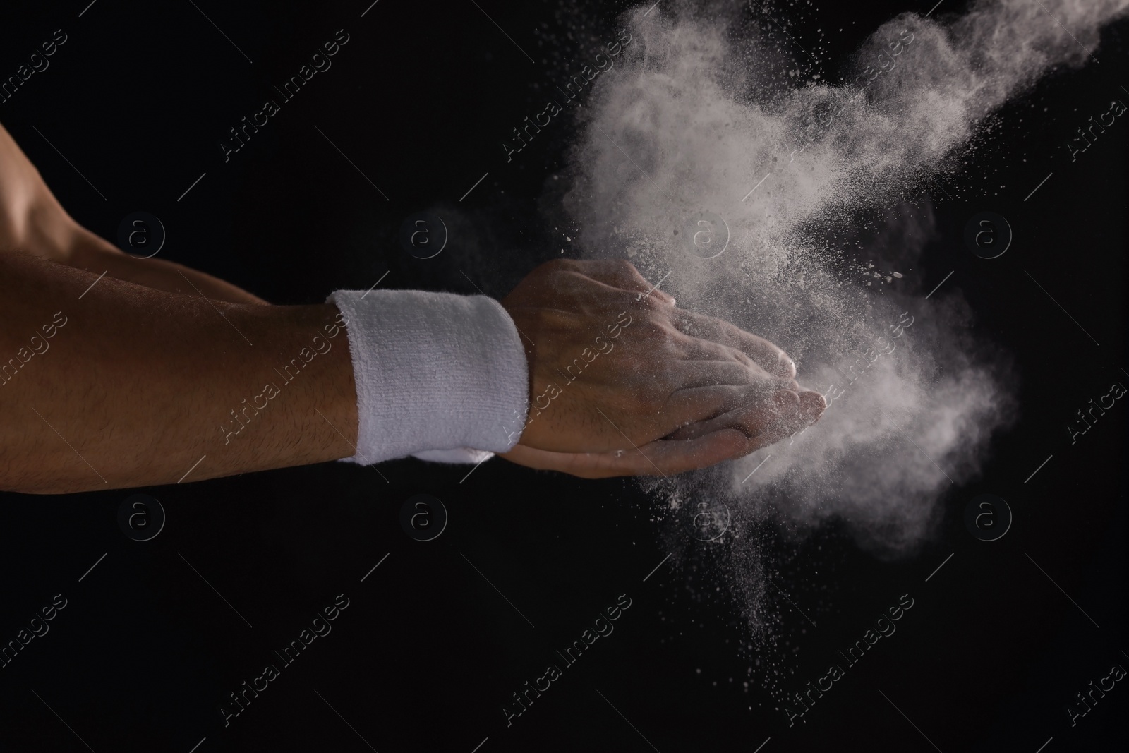 Photo of Young man applying chalk powder on hands against dark background