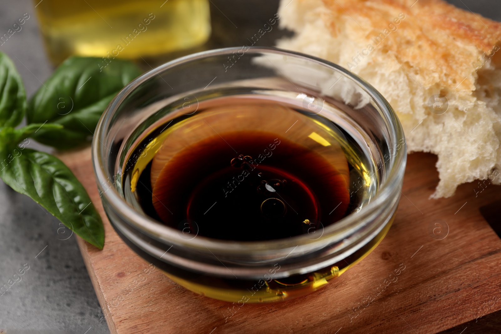 Photo of Bowl of organic balsamic vinegar with oil, basil and bread on grey table, closeup