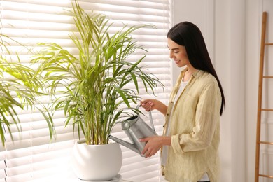 Photo of Young woman watering house plant on window sill indoors