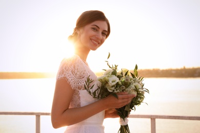 Photo of Gorgeous bride in beautiful wedding dress with bouquet near river on sunset