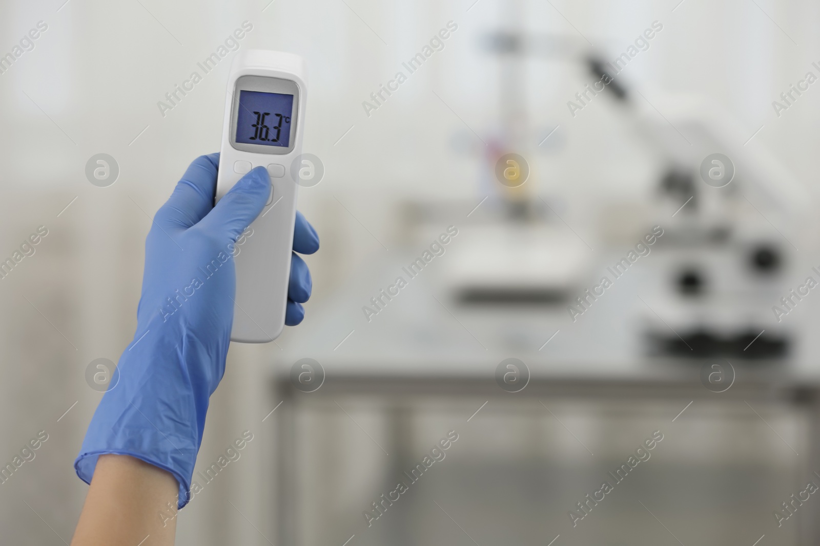 Photo of Closeup view of doctor with infrared thermometer on blurred background, space for text. Checking temperature during Covid-19 pandemic