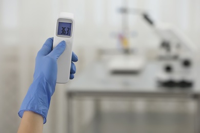 Photo of Closeup view of doctor with infrared thermometer on blurred background, space for text. Checking temperature during Covid-19 pandemic