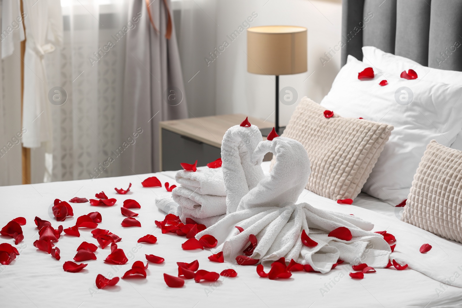 Photo of Honeymoon. Swans made with towels and beautiful rose petals on bed in room