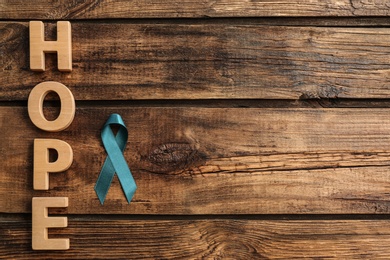 Photo of Word Hope made of letters and teal awareness ribbon on wooden background, top view. Symbol of social and medical issues