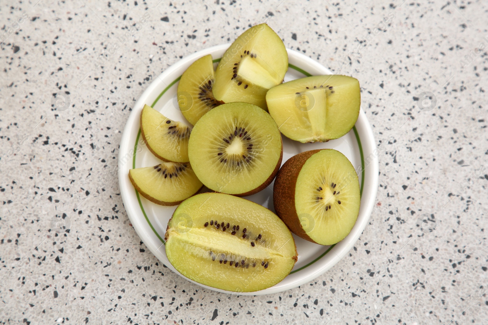 Photo of Plate of cut fresh kiwis on white table with pattern, top view