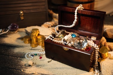 Photo of Chest with treasures and scattered sand on wooden table