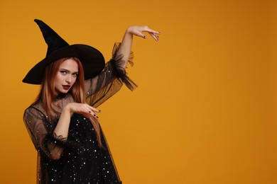 Happy young woman in scary witch costume posing on orange background, space for text. Halloween celebration